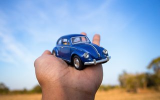 Eine Hand hält ein blaues Spielzeugauto vor blauem Himmel im Freien.